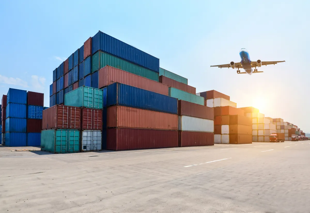 Stacked shipping containers at a freight terminal with a cargo plane overhead