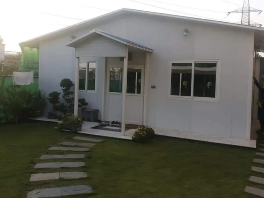 White single-storey prefabricated home with a gabled porch and landscaped garden path